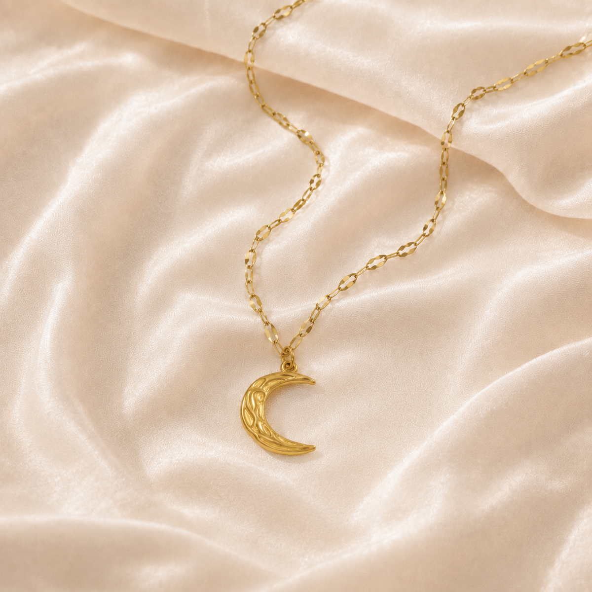 Warm gold-toned asymmetrical crescent pendant necklace on cream silk
