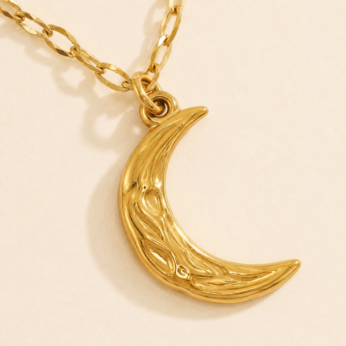 Close-up of the raised and recessed relief channels on the warm gold-toned crescent pendant