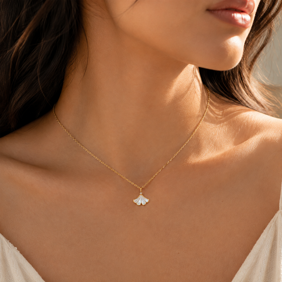 Editorial chest-up view wearing a fine warm-tone chain with a pale fan-shaped leaf pendant