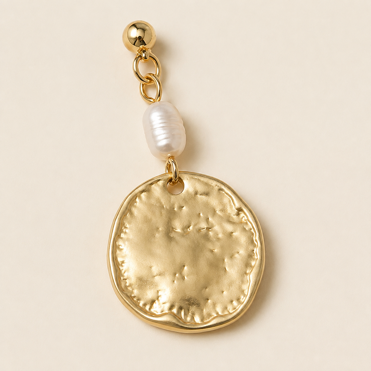 Close view of one pale oval pearl element above a hammered-looking warm-tone disc