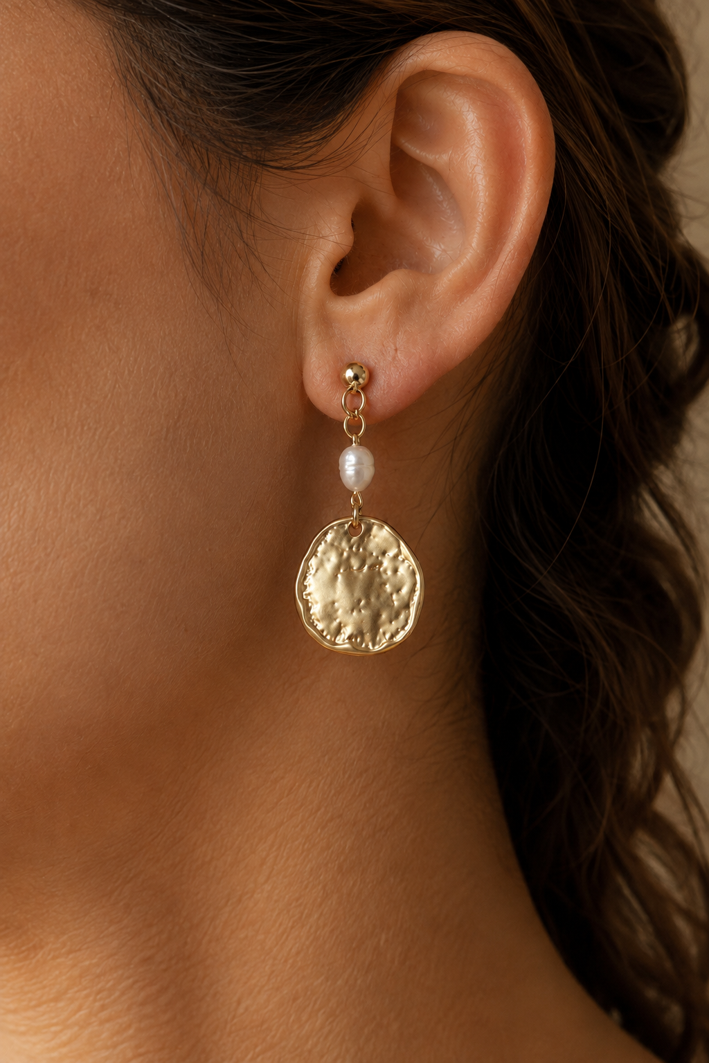 Close ear view wearing a pearl element and textured disc drop earring