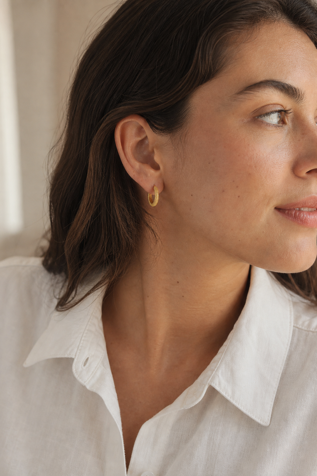 Gold-tone textured huggie earring worn on an ear