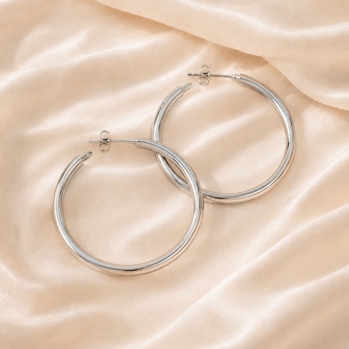 Pair of silver-tone sculpted hoop earrings on warm cream silk