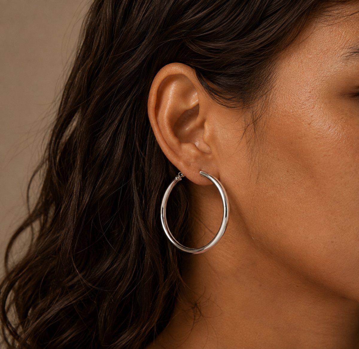 Silver-tone sculpted hoop earring worn on ear, showing its circular form and broad front arc