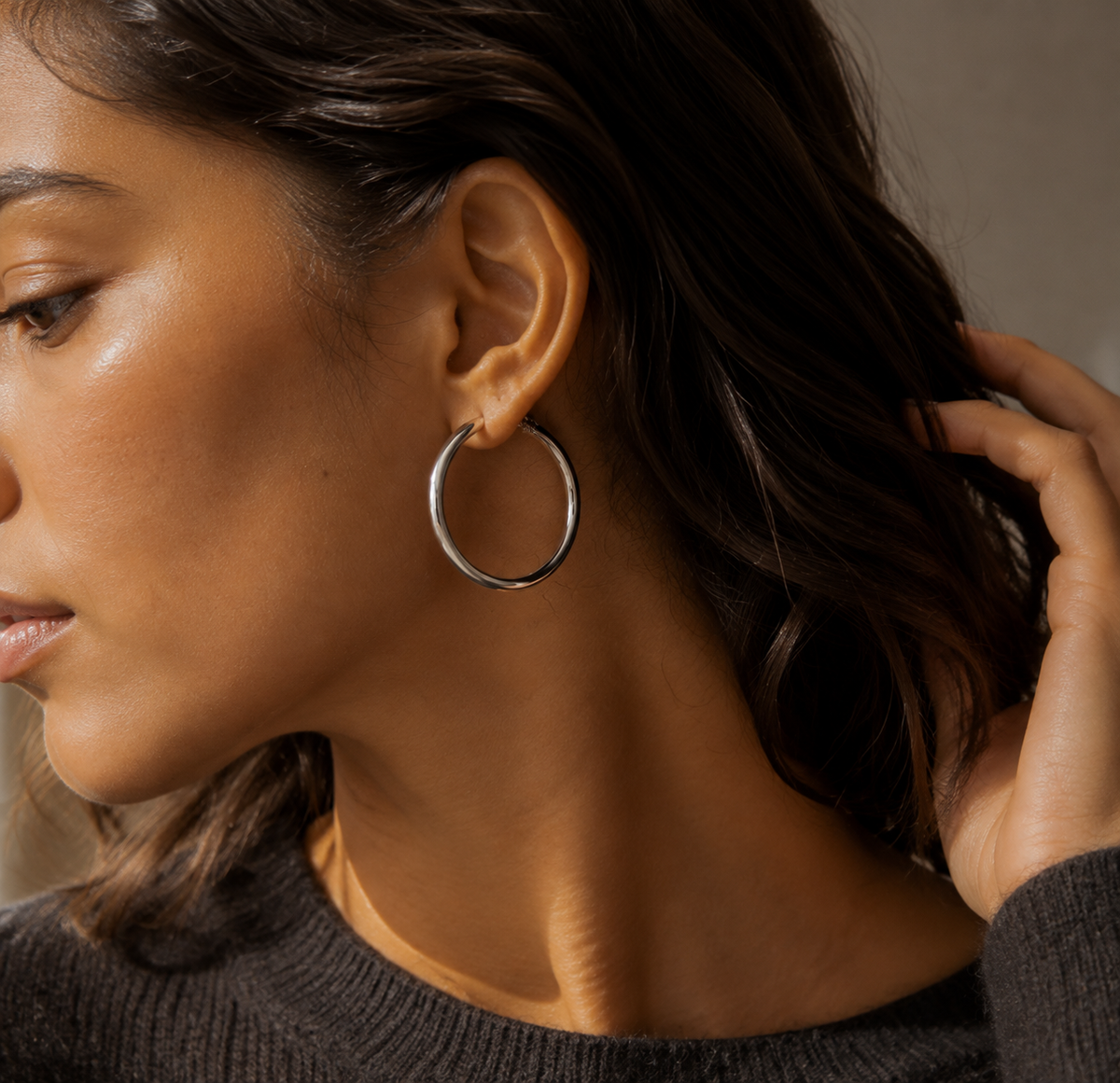 Second worn editorial view of a silver-tone sculpted hoop earring with a slim rear arc
