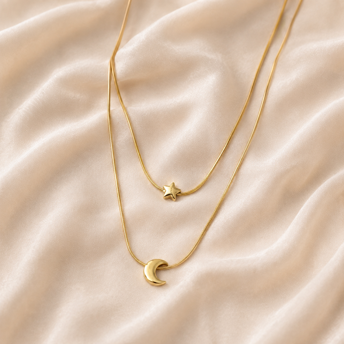 Two-layer gold-toned celestial necklace with a small star above a right-opening crescent on cream silk.