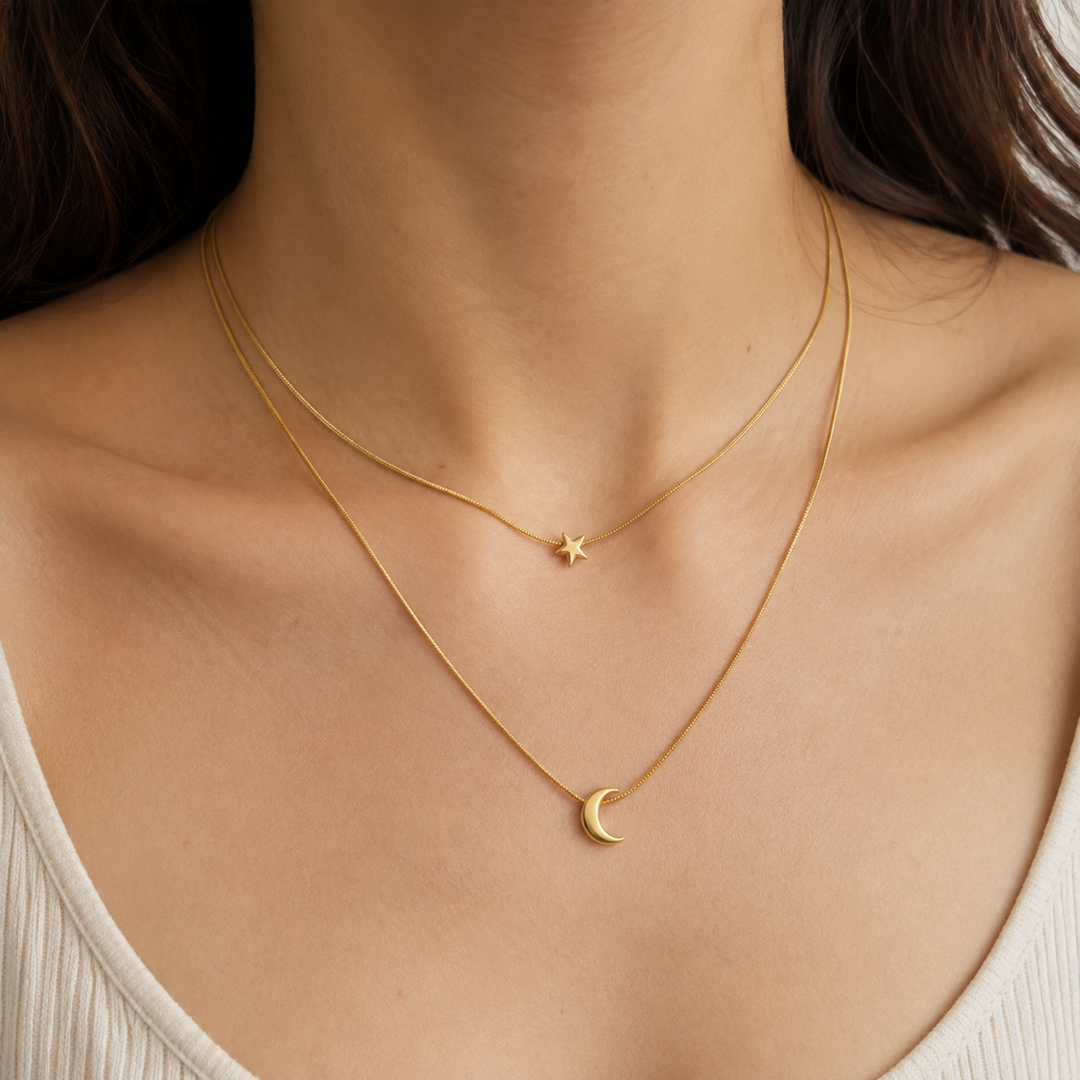 Close neck and collarbone view of a two-layer gold-toned necklace with a star above a right-opening crescent.