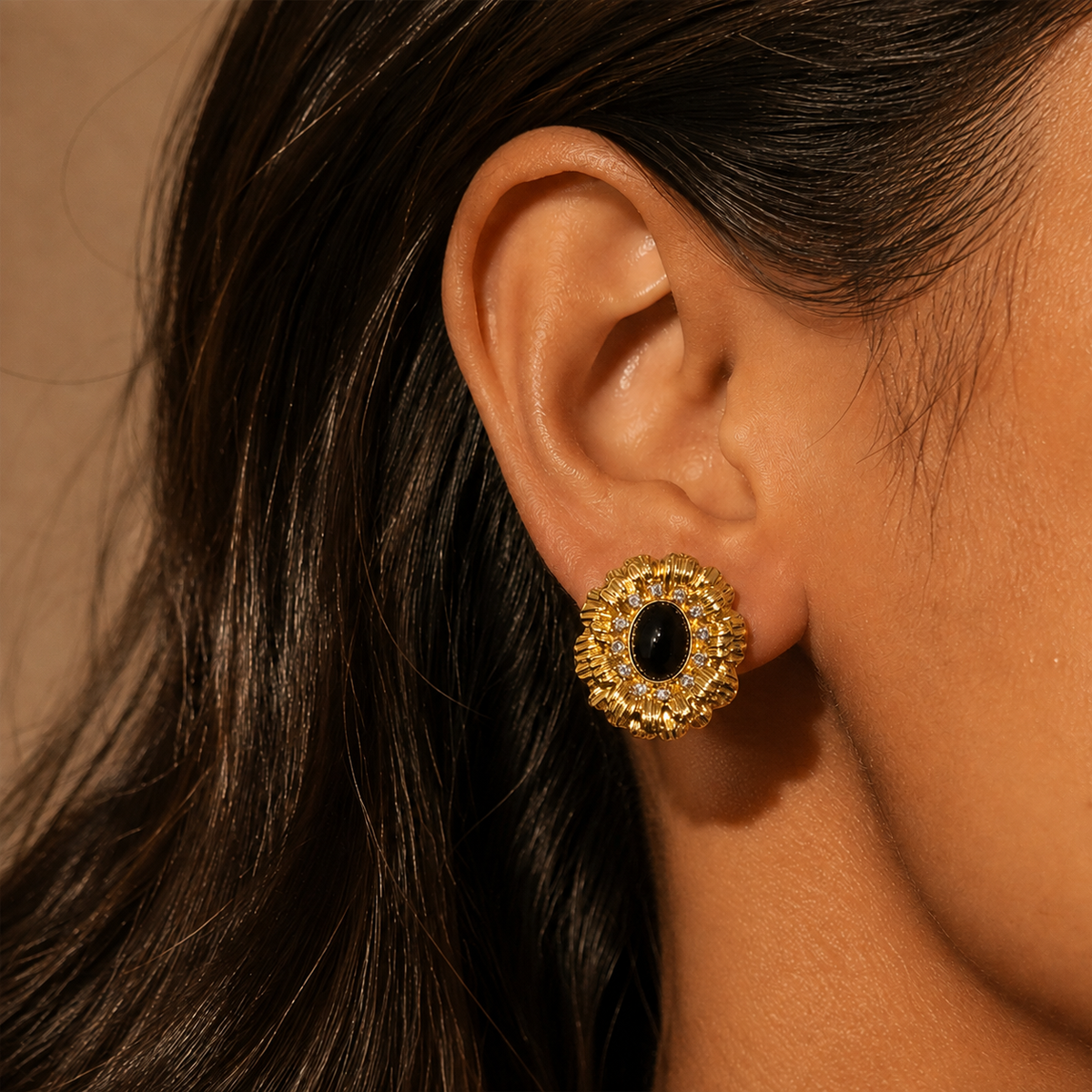 Gold-tone ridged radiating earring with a dark oval center shown on an ear in a close editorial view