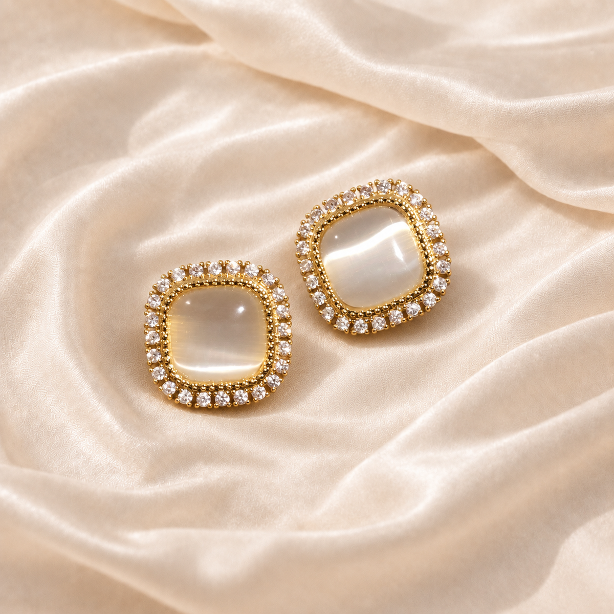 Pair of Soft Geometry Stud Earrings with pale rounded-square centers and clear-looking halos on cream silk