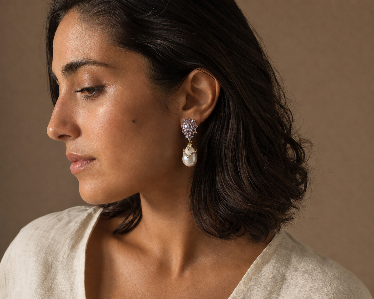 Side-profile editorial view of a violet faceted drop earring with a chevron frame over a smooth white pear-shaped pearl drop.