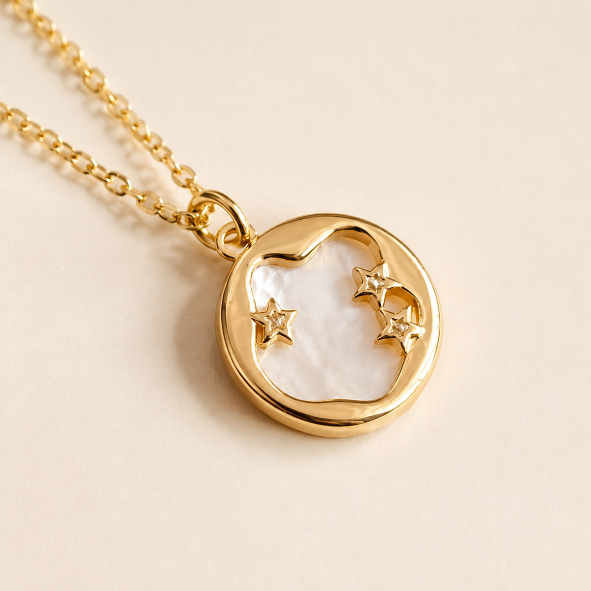 Close-up of Aster Crest's round pale pearlescent pendant with a gold-tone crescent-like arc and three stars