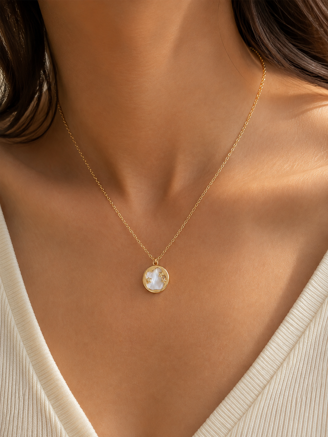 Aster Crest pendant necklace worn in a close editorial view, showing its pale round center and gold-tone celestial details