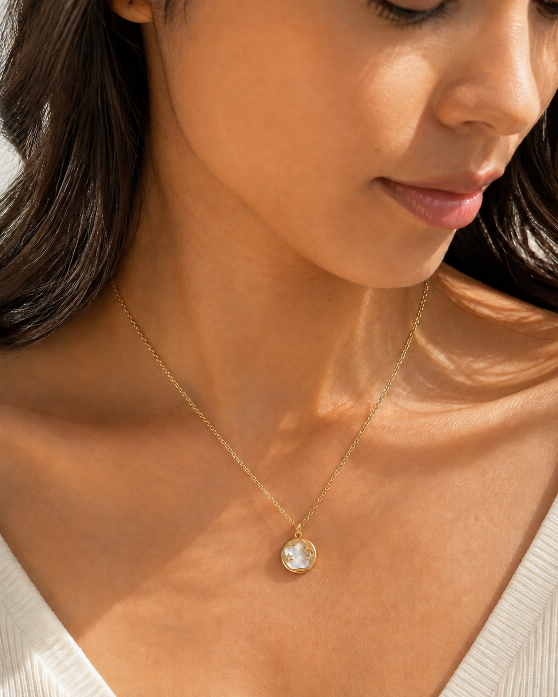Aster Crest pendant necklace in an off-axis editorial view, showing the round pale pearlescent center and three stars