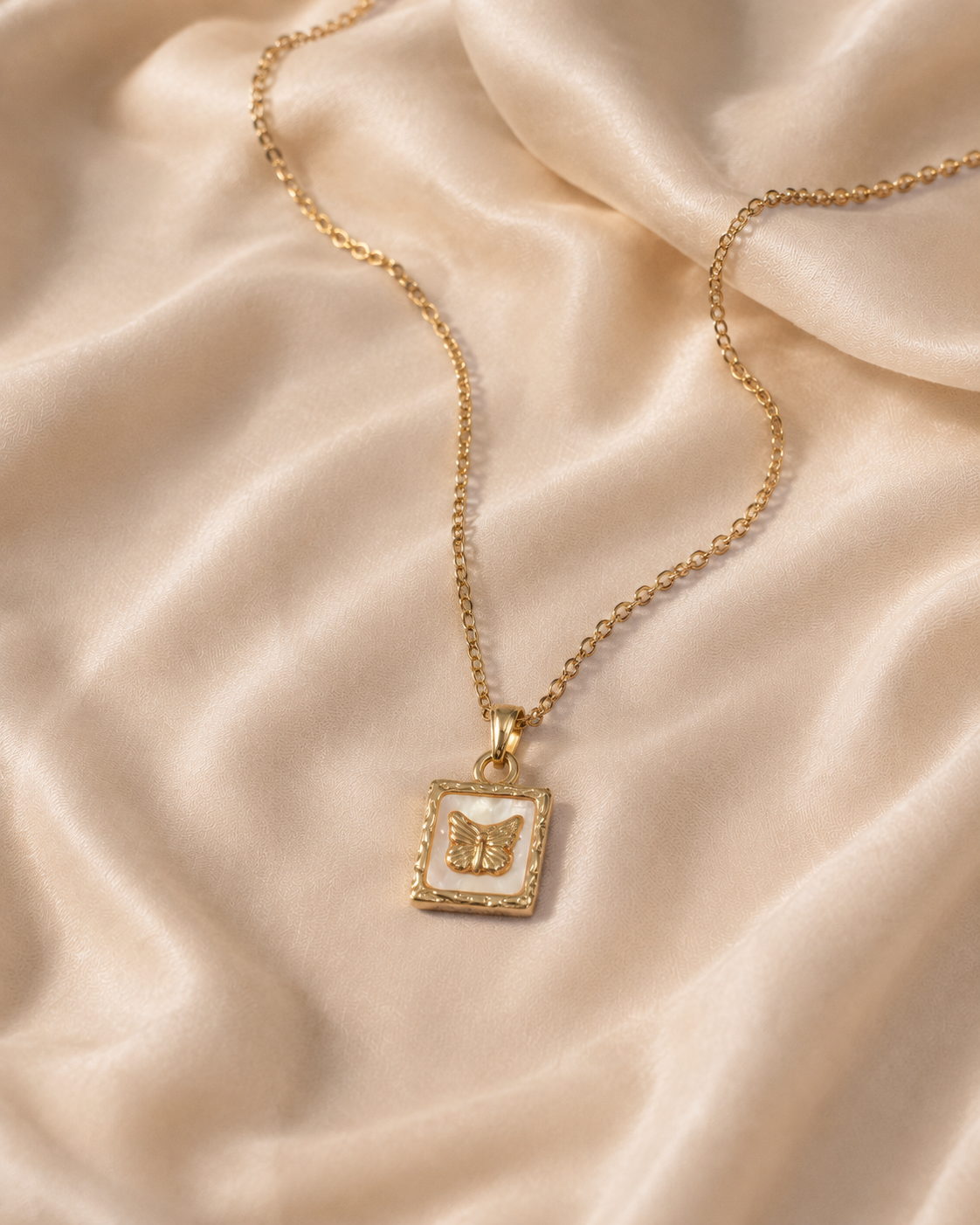 Butterfly Memento Pendant Necklace with a pale rectangular inset and textured warm yellow-gold-toned frame on cream silk.