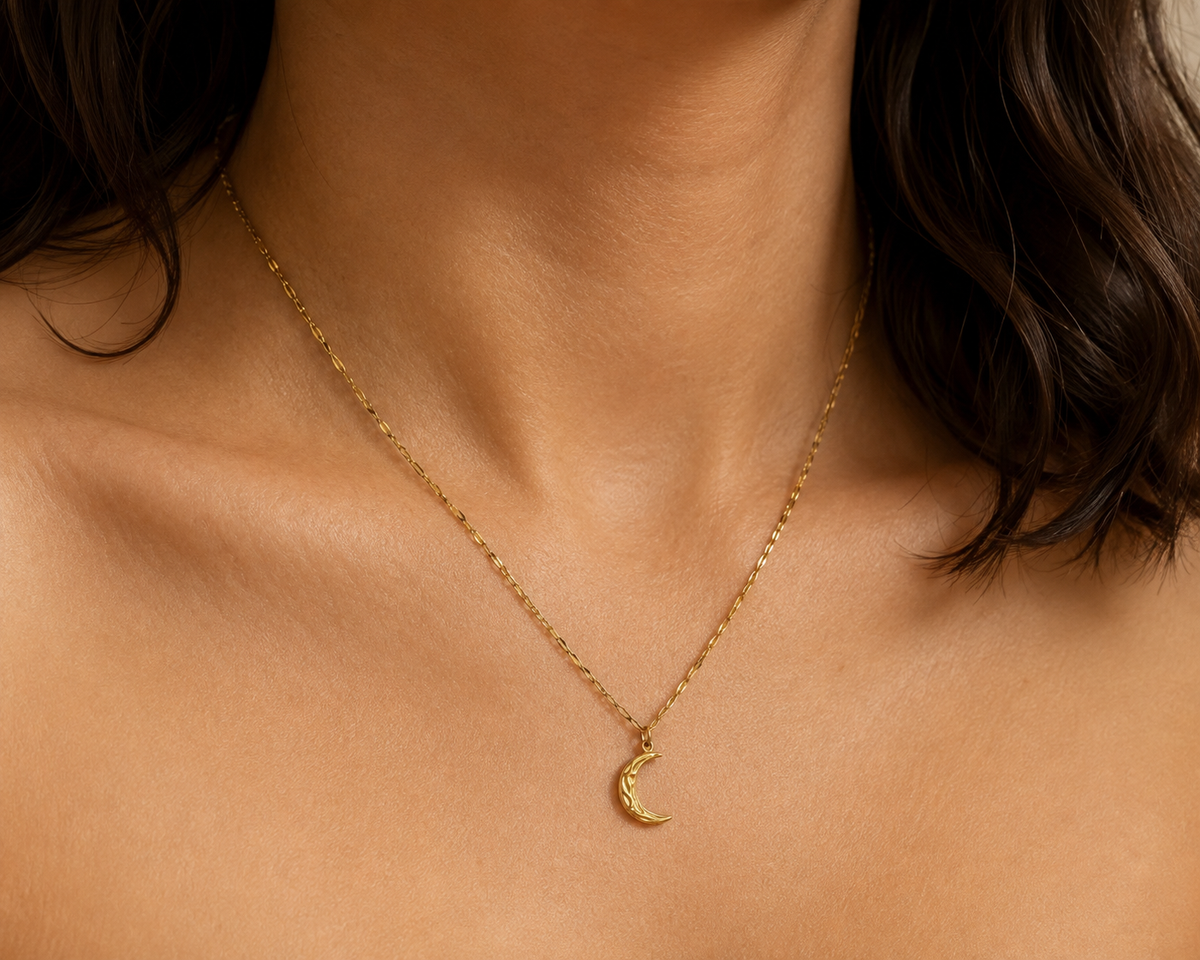 Warm gold-toned asymmetrical crescent pendant necklace worn in an editorial view