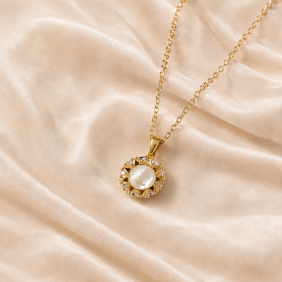 Aureole Inlay Pendant Necklace with a warm gold-toned chain, pale iridescent-looking round centre, and clear faceted halo on cream silk.