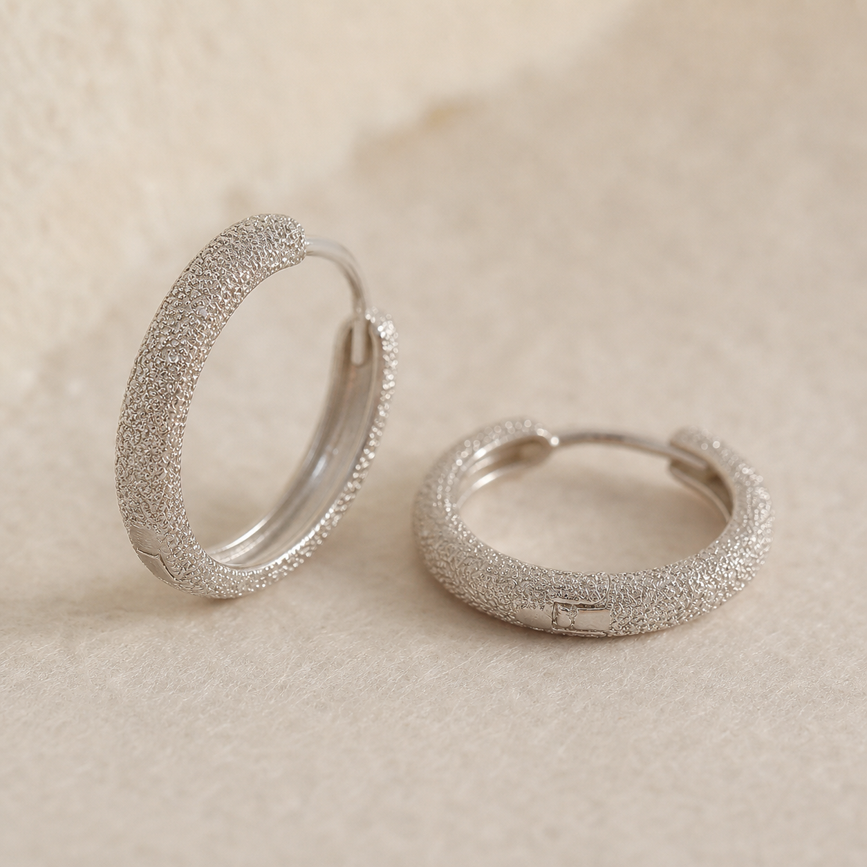 Silver-tone huggie earrings showing granular texture and hinged closure