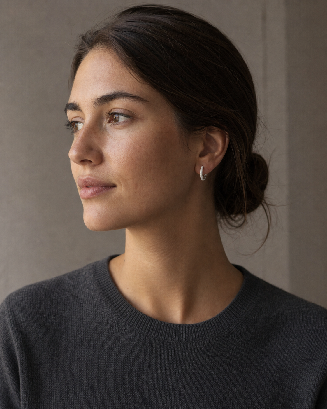 Silver-tone textured huggie earring worn in a wider portrait