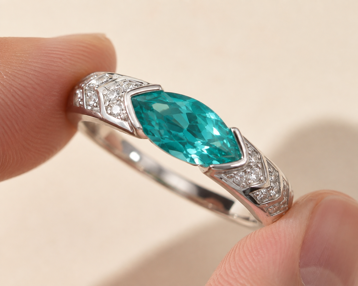 Close view of a closed silver-tone ring with a blue-green center and mirrored stepped shoulders