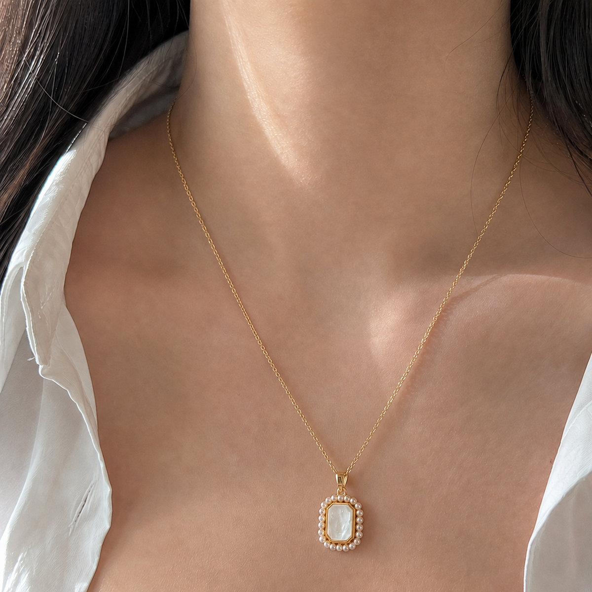 Close upper-chest view of the Folio Frame Pendant Necklace on a fine warm yellow-gold-toned chain