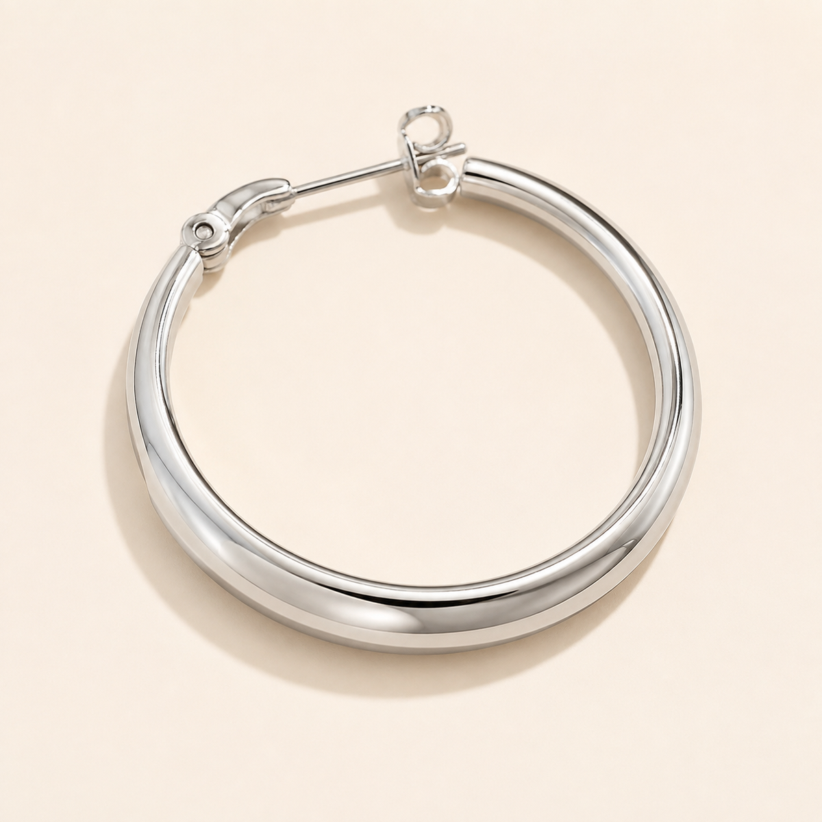 Close-up of a silver-tone sculpted hoop earring with a smooth reflective front arc