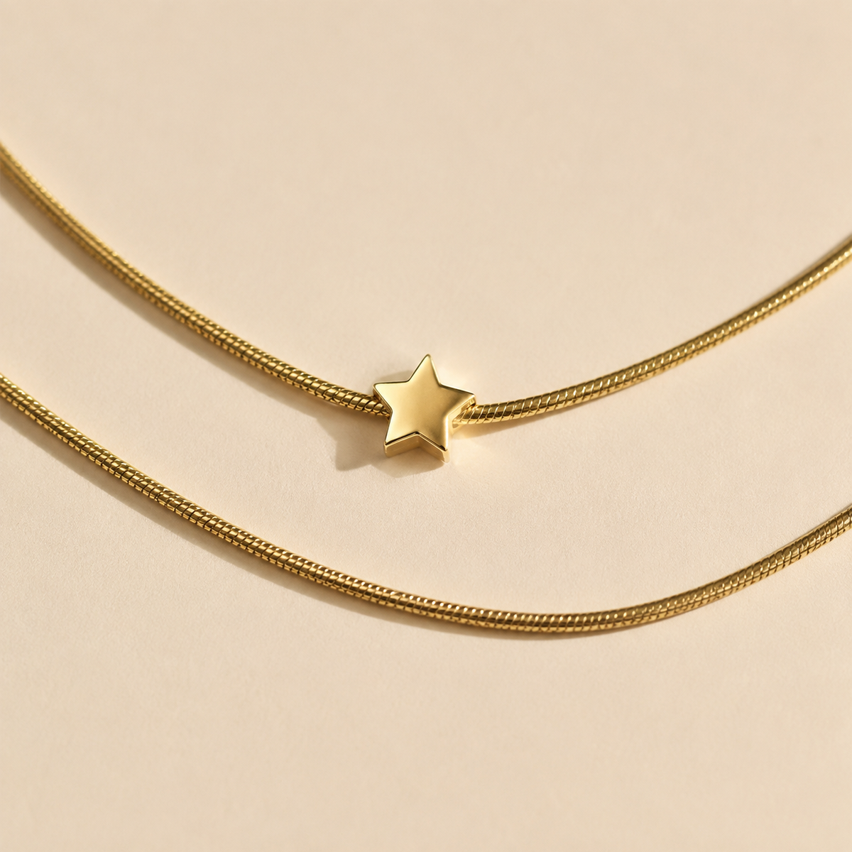 Close-up of a small star and two separate fine gold-toned necklace strands on a light cream background.