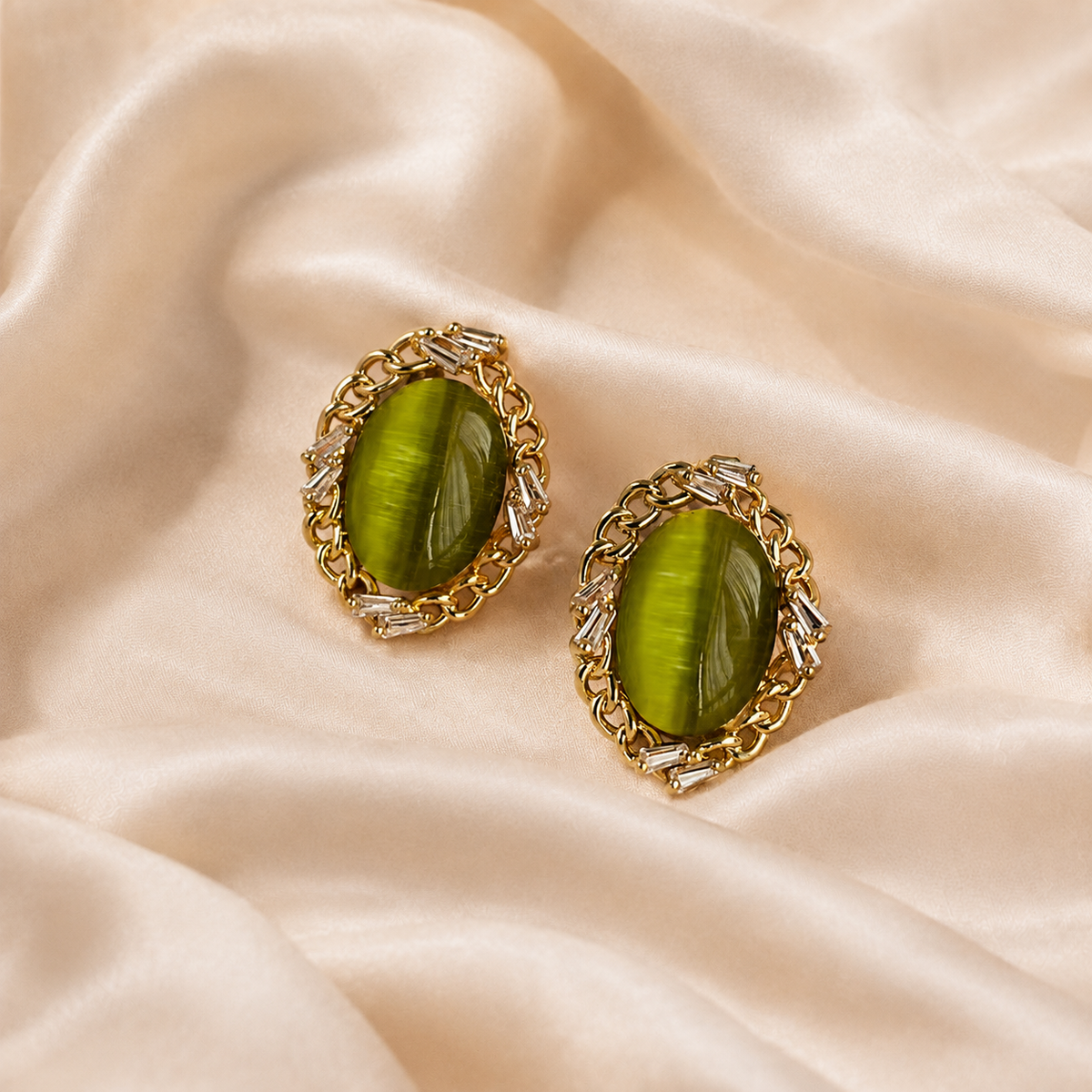 Pair of green oval stud-front earrings with metallic borders on warm cream silk