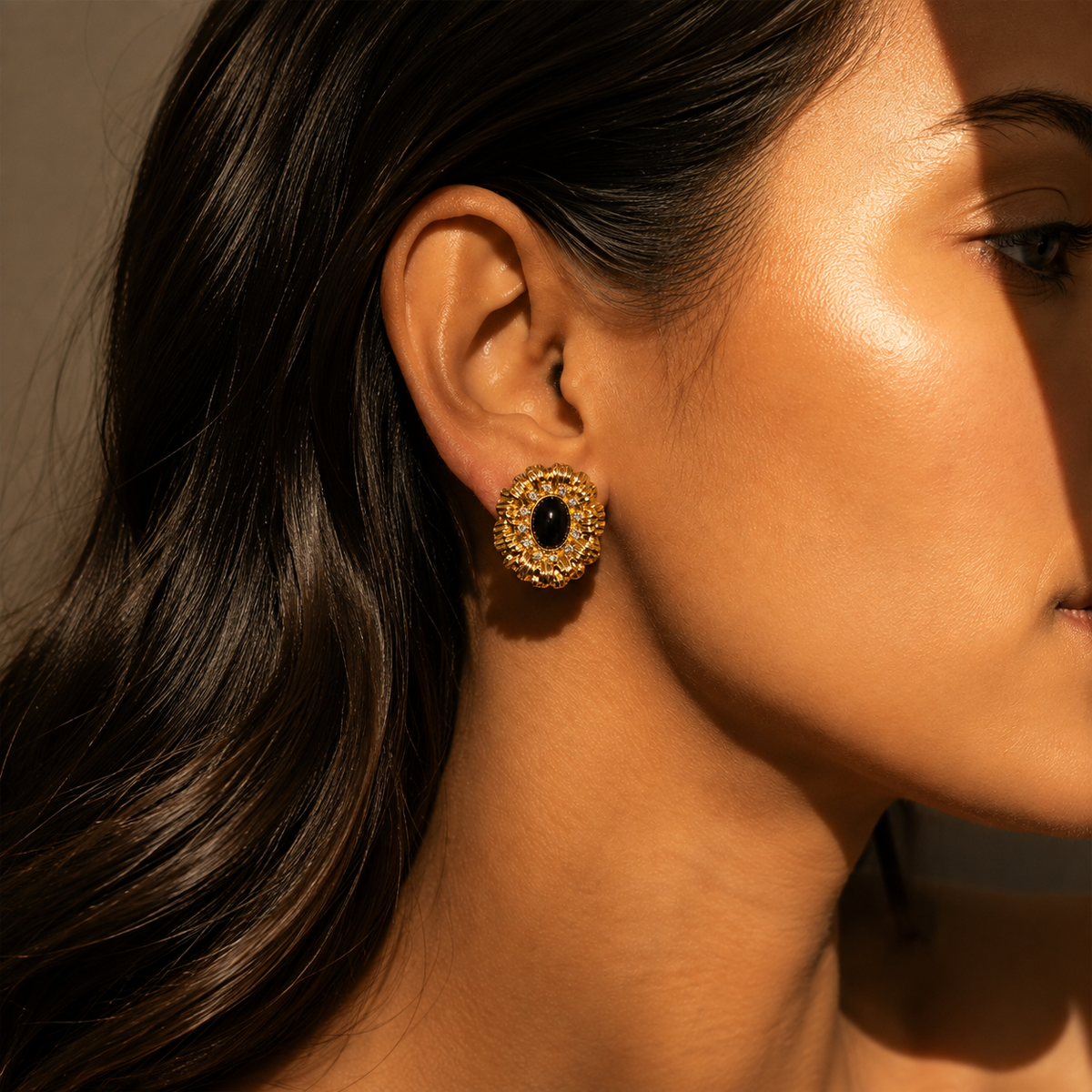 Gold-tone ridged radiating earring with a dark oval center in a side-profile editorial view
