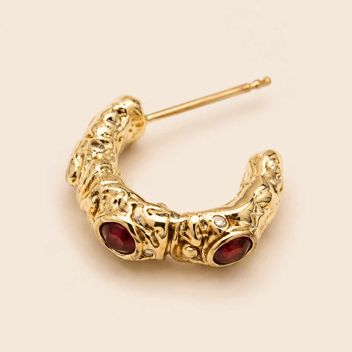 Close view of an open C-shaped earring with red and clear-looking front details