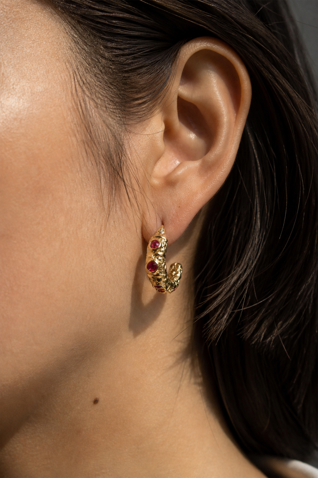 Close ear view wearing a compact open-curve earring with deep red accents