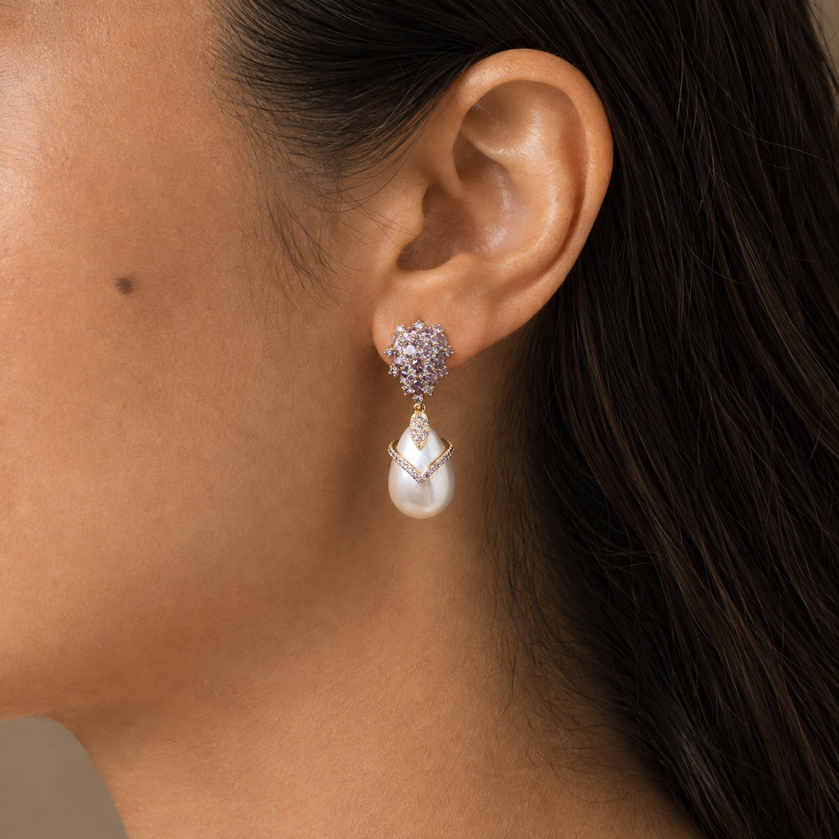 Close ear view of a violet faceted drop earring with a round link, faceted connector, and smooth white pear-shaped pearl drop.